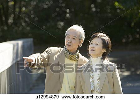 Stock Photo - A Mature Couple Pointing Away and Talking, Front View, Waist Up. Fotosearch