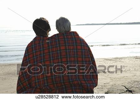 Stock Image - A Mature Couple Wrapped up in a Blanket Together, Rear View, Waist Up. Fotosearch