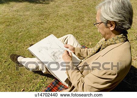Stock Image - A Mature Man Sketching on the Lawn, Side View, High Angle View. Fotosearch