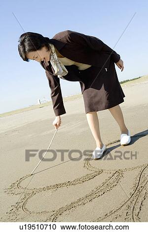 Stock Image - A Mature Woman Scribbling on the Beach, Full Length, Side View. Fotosearch