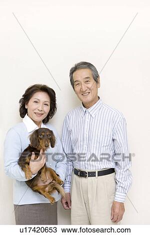 Stock Image - A Portrait of a Senior Adult Coupe Smiling at Camera with a Dog, Front View. Fotosearch