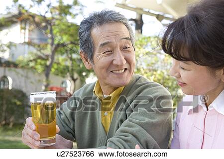Stock Photograph - A Senior Adult Couple Drinking Beer in a Garden, Side View, Differential Focus. Fotosearch