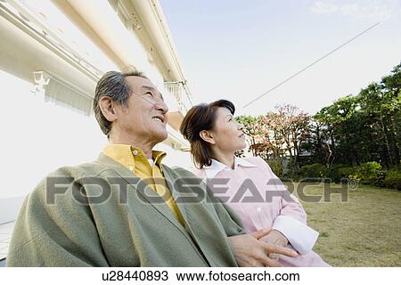 Stock Image - A Senior Adult Couple Relaxing in a Garden, Side View, Low Angle View. Fotosearch