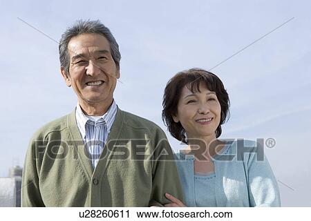 Stock Image - A Senior Adult Couple Smiling Under the Sky, Front View. Fotosearch