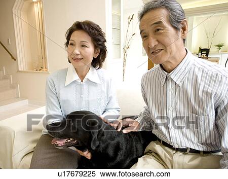 Stock Photography - A Senior Adult Couple Smiling with a Dog in a Living Room, Side View. Fotosearch