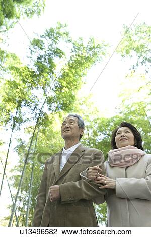 Stock Image - A Senior Adult Couple Walking Together in a Bamboo Forest, Low Angle View. Fotosearch