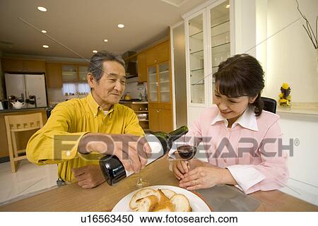 Stock Image - A Senior Adult Man Pouring Some Wine for His Wife, Front View, Side View. Fotosearch