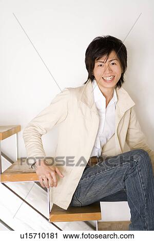Stock Image - A Young Adult Man Sitting on Stairs and Smiling at Camera, Side View, Front View. Fotosearch