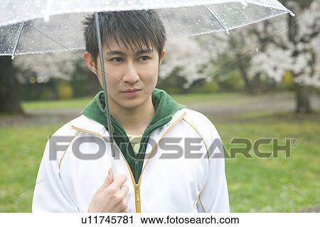 Stock Image - Portrait of a man holding an umbrella, front view, Japan. Fotosearch