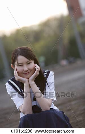 Stock Photograph - Portrait of a teenage girl sitting and resting chin in hands in schoolyard, smiling and looking at camera. Fotosearch