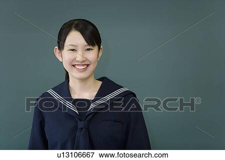 Stock Photo - Portrait of a teenage girl standing in front of blackboard, smiling and looking at camera, green background. Fotosearch