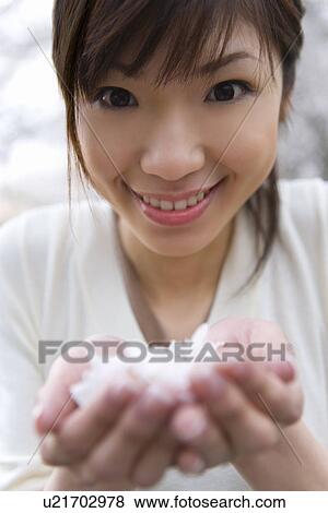 Stock Photo - Portrait of a woman scooping up cherry flowers with hands, smiling and looking at camera, front view, close up, Japan. Fotosearch