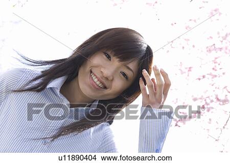 Picture - Portrait of a woman standing under the cherry tree, smiling and looking at camera, low angle view, white background, Japan. Fotosearch