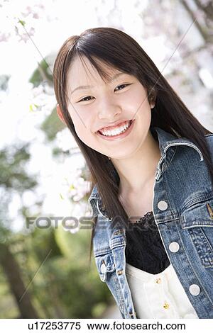 Stock Photography - Portrait of a woman standing under the cherry tree, smiling and looking at camera, front view, Japan. Fotosearch