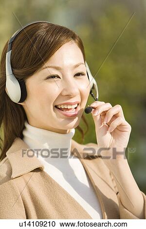 Stock Image - Portrait of a woman wearing a hands-free headset, front view, differential focus. Fotosearch