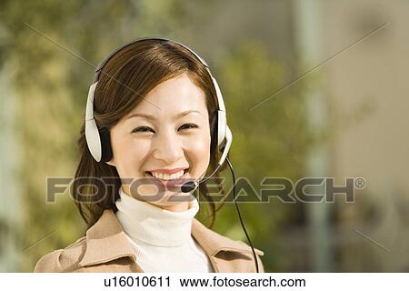 Stock Image - Portrait of a woman wearing a hands-free headset, looking at camera, front view, differential focus. Fotosearch