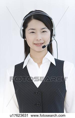 Stock Image - Portrait of a woman wearing hands-free headset, looking at camera, front view, white background. Fotosearch