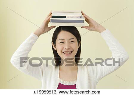 Stock Image - Portrait of a Young Woman Balancing Books on Her Head, Smiling, Front View. Fotosearch