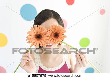 Portrait of a Young Woman Covering Her Eyes with Flowers of Gerbera, Smiling, Front View View Large Photo Image Stock Photography - Portrait of a Young Woman Covering Her Eyes with Flowers of Gerbera, Smiling, Front View. Fotosearch
