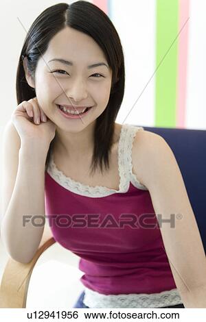 Stock Photograph - Portrait of a Young Woman Sitting with Her Hand under the Chin, Front View. Fotosearch