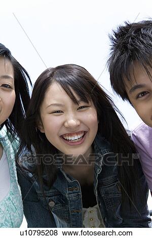Stock Photo - Portrait of three young people, smiling and looking at camera, front view, white background, Japan. Fotosearch