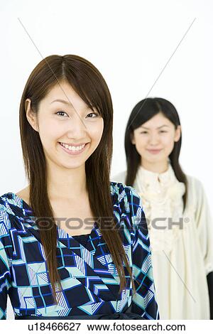 Stock Photo - Portrait of two women smiling and looking at camera, front view, white background. Fotosearch