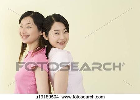 Portrait of Two Young Twin Sisters Back to Back, Smiling, Side View, Copy Space View Large Photo Image Picture - Portrait of Two Young Twin Sisters Back to Back, Smiling, Side View, Copy Space. Fotosearch