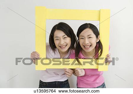 Portrait of Two Young Twin Sisters Holding a Picture Frame, Smiling, Front View View Large Photo Image Picture - Portrait of Two Young Twin Sisters Holding a Picture Frame, Smiling, Front View. Fotosearch