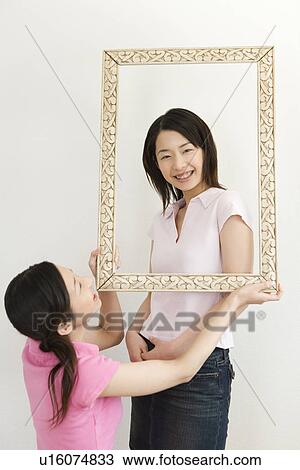 Portrait of Two Young Twin Sisters, Holding and Looking Through a Picture Frame, Smiling, Front View, Rear View View Large Photo Image Stock Image - Portrait of Two Young Twin Sisters, Holding and Looking Through a Picture Frame, Smiling, Front View, Rear View. Fotosearch
