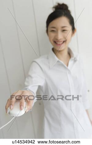 Stock Image - Woman smiling and holding computer mouse, front view, differential focus. Fotosearch