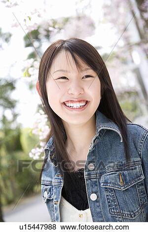 Stock Photo - Woman smiling and standing under the cherry tree, front view, Japan. Fotosearch