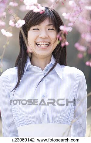 Stock Image - Young Woman and Weeping Cherry Trees, Differential Focus, Front View. Fotosearch