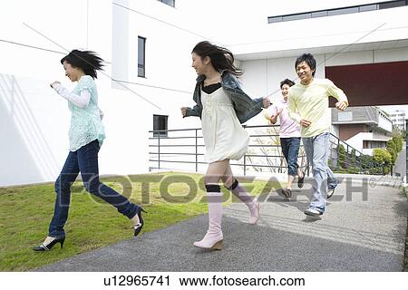Stock Image - Four young people running in campus, front view, side view, Japan. Fotosearch