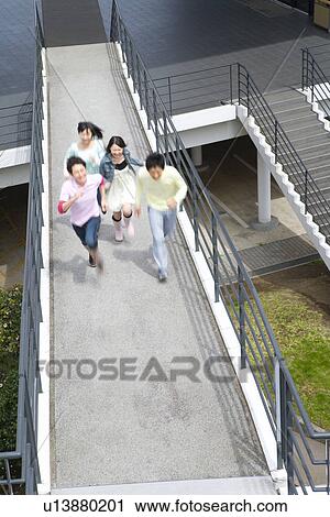 Stock Image - Four young people running on footbridge, high angle view, blurred motion, Japan. Fotosearch
