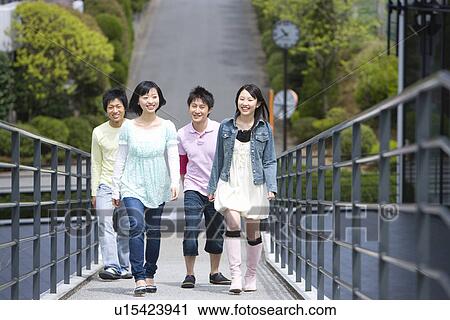 Stock Image - Four young people walking on footbridge, smiling, front view, Japan. Fotosearch