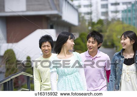 Stock Image - Four young people walking on footbridge, smiling, front view, Japan. Fotosearch