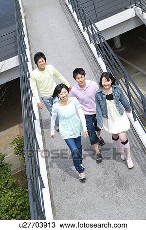 Stock Image - Four young people walking on footbridge, smiling, high angle view, Japan. Fotosearch