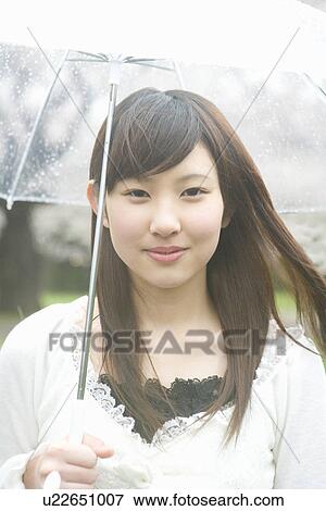 Stock Photo - Portrait of a woman holding an umbrella, smiling and looking at camera, front view, Japan. Fotosearch