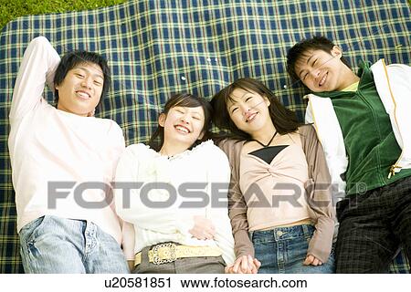 Stock Image - Portrait of four young people lying on sheet, smiling and looking at camera, high angle view, Japan. Fotosearch