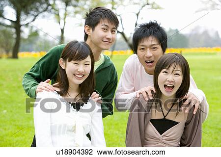 Stock Image - Portrait of four young people on lawn, smiling and looking at camera, front view, Japan. Fotosearch