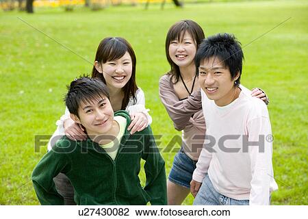 Stock Image - Portrait of four young people on lawn, smiling and looking at camera, front view, Japan. Fotosearch