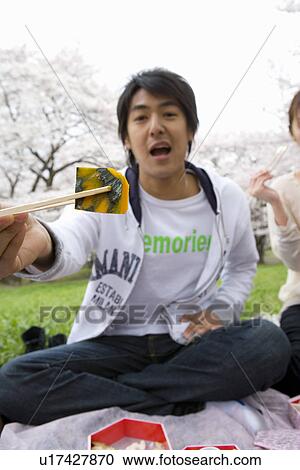 Stock Image - Portrait of man holding squash with chopsticks, looking at camera, front view, Japan. Fotosearch