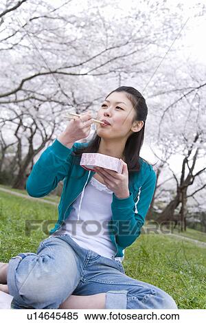 Stock Photography - Woman enjoying lunch surrounded with cherry blossoms, front view, Japan. Fotosearch