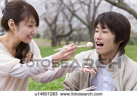Stock Image - Woman feeding man aroid with chopsticks, smiling, front view, side view, Japan. Fotosearch