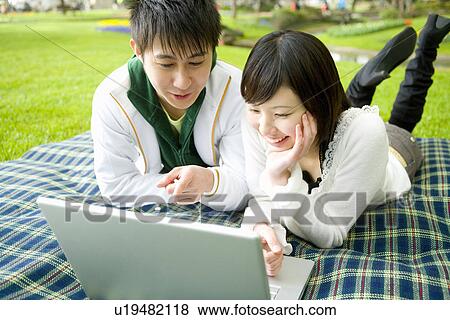 Young couple looking at laptop, lying on sheet, front view, Japan View Large Photo Image Stock Photo - Young couple looking at laptop, lying on sheet, front view, Japan. Fotosearch