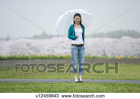 Stock Image - Young Woman and Cherry Blossoms in the Background, Differential Focus, Front View. Fotosearch