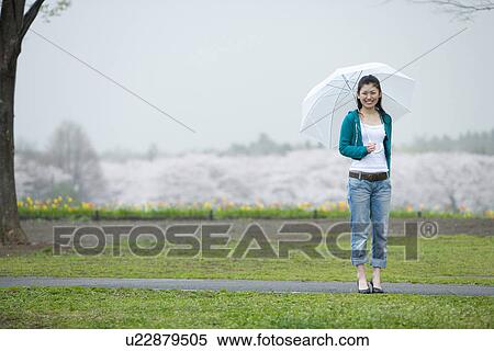 Stock Photography - Young Woman and Cherry Blossoms in the Background, Front View. Fotosearch