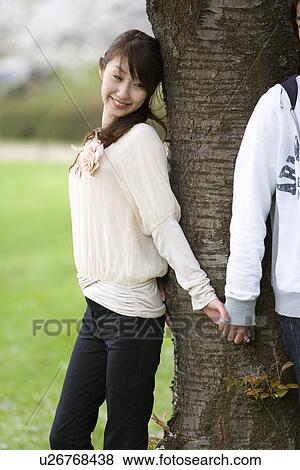 Stock Photo - Young Woman Holding Hands With Man's Beneath a Tree, Side View. Fotosearch