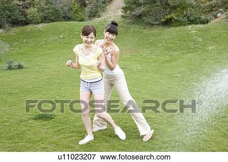 Young woman spraying water to friends, high angle view View Large Photo Image Stock Photo - Young woman spraying water to friends, high angle view. Fotosearch