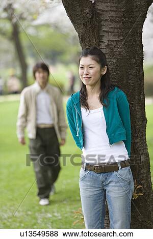 Stock Photo - Young Woman Standing Beneath a Tree, Differential Focus, . Fotosearch